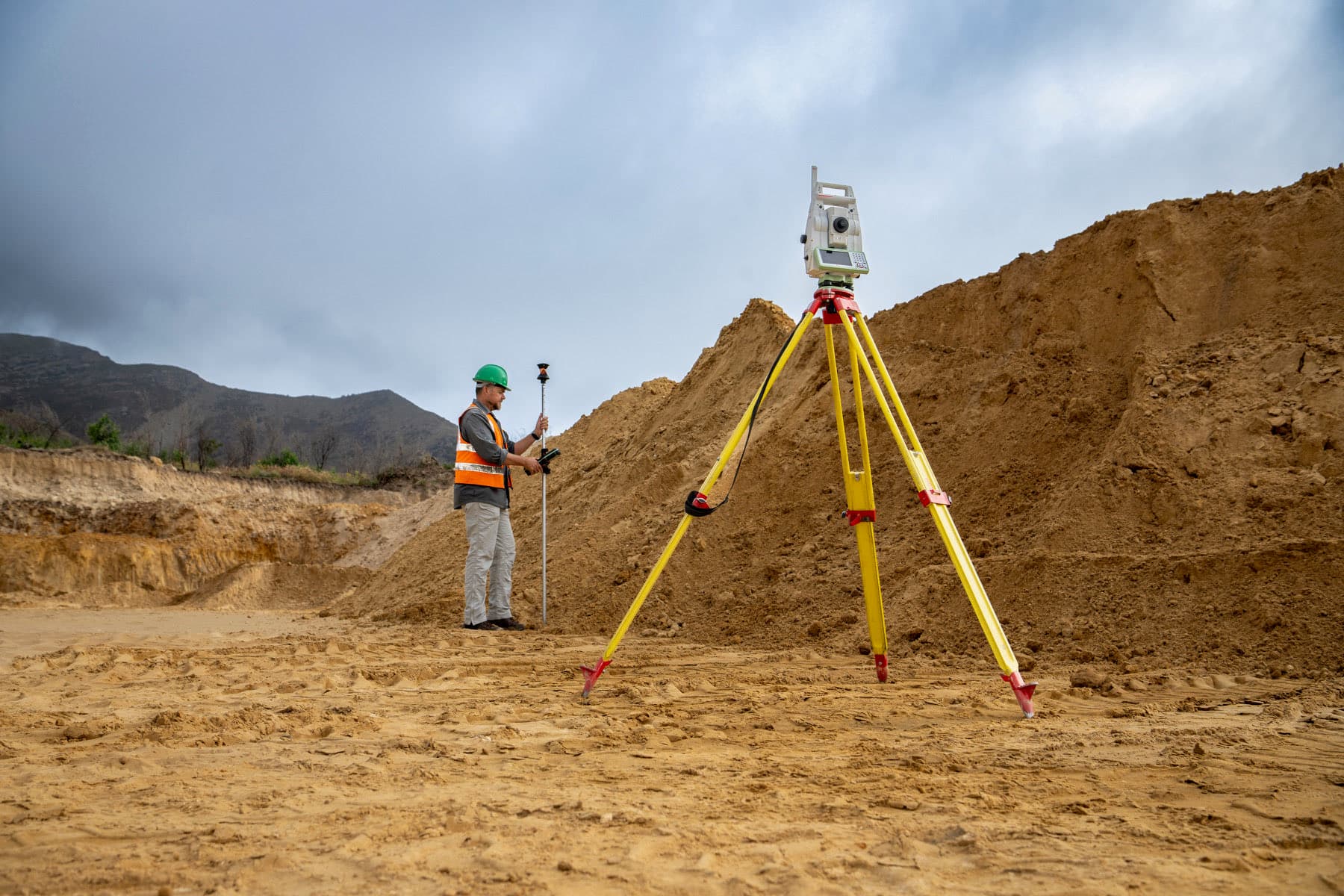 A GeoSurv surveyor holding a prism pole beside a total station on site.